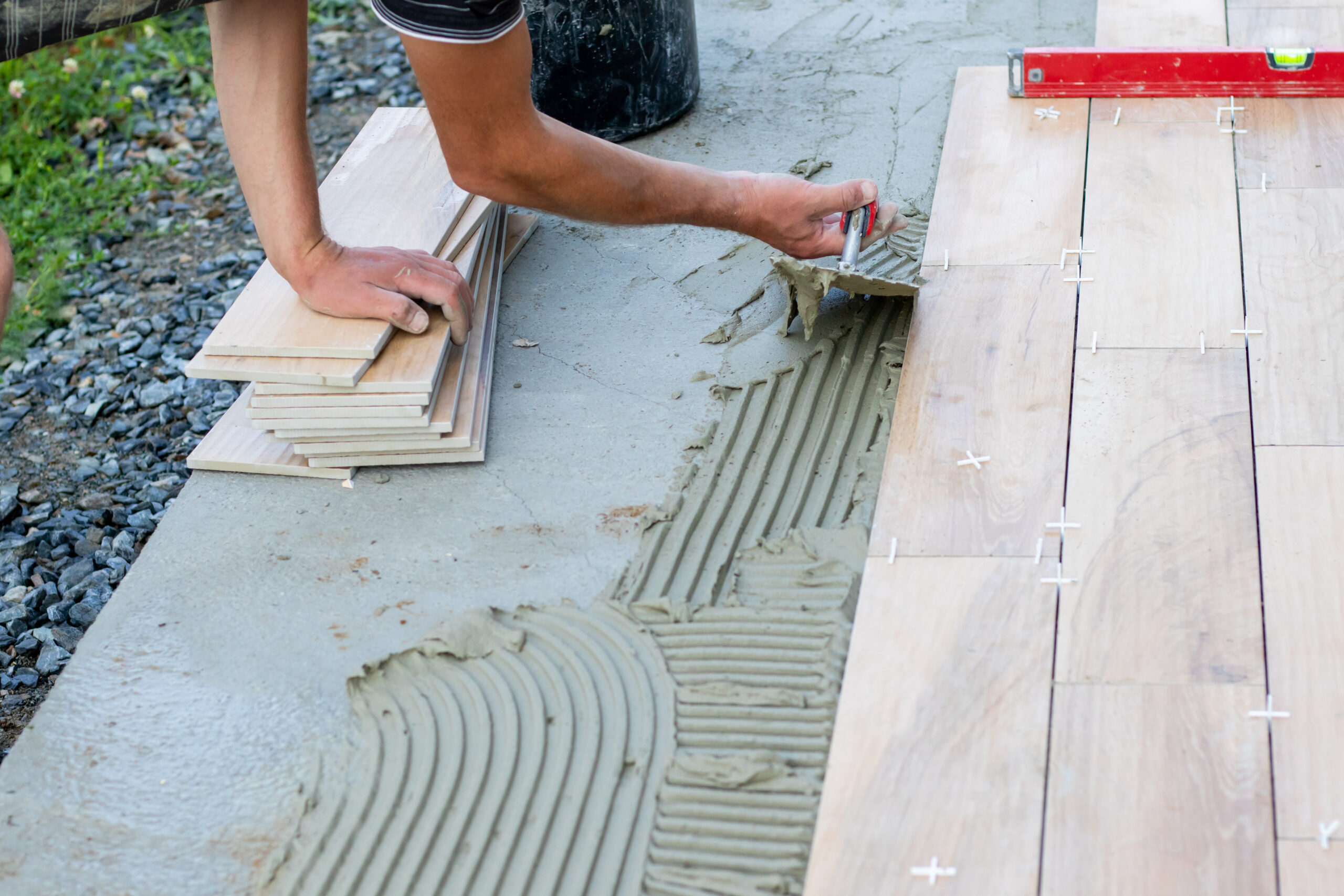 The hands of the professional tiler lying or installing modern, ceramic tile above cement on the garden terrace , tiling floor, building and pavement concept